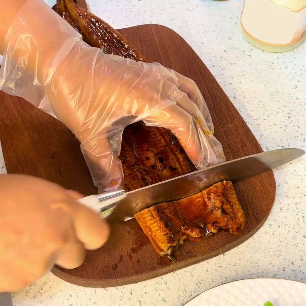 Un cuchillo cortando un trozo de anguila a la parrilla sobre una tabla de cortar de madera.