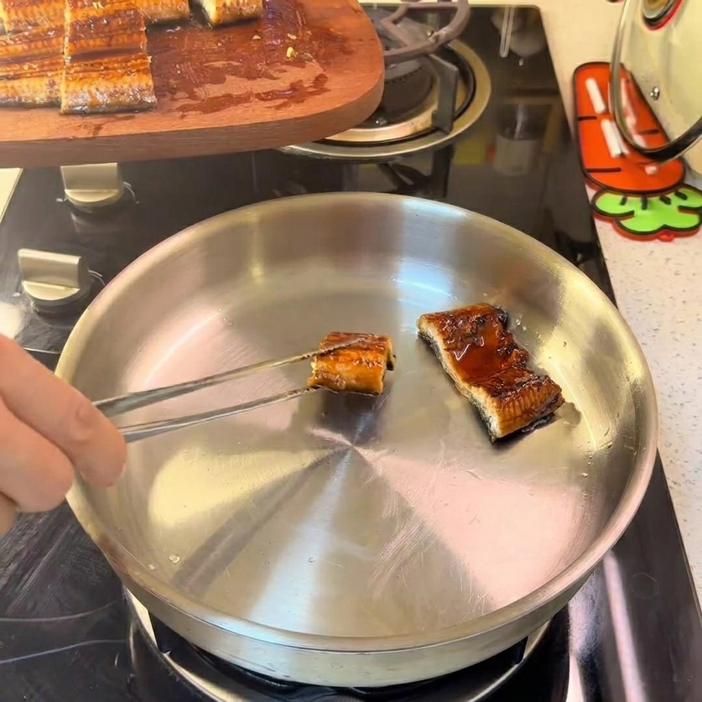 Trozos de anguila dispuestos en una sartén de acero inoxidable, salteándose suavemente a fuego lento.