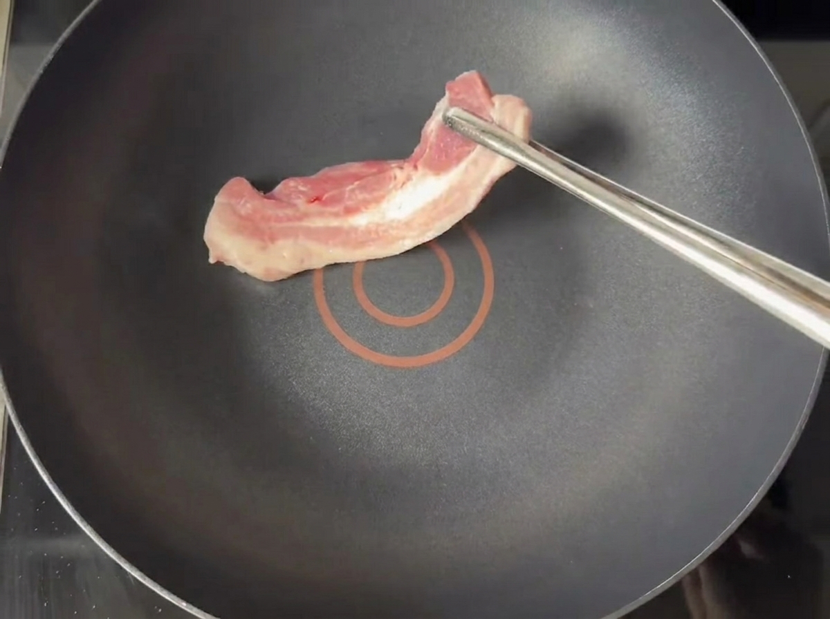 Tiras de panceta de cerdo dorándose en una sartén antiadherente seca.