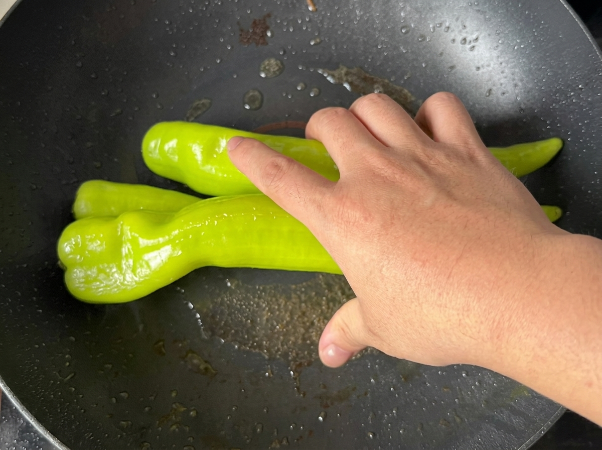 Pimientos verdes friéndose en una sartén hasta que la piel se vuelve ampollada y carbonizada.