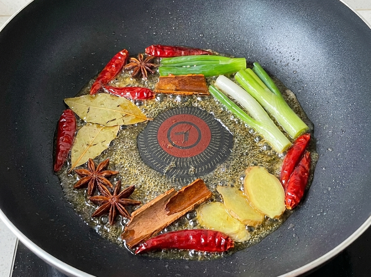 Una mezcla de cebolletas, chiles secos y especias enteras friéndose en aceite.