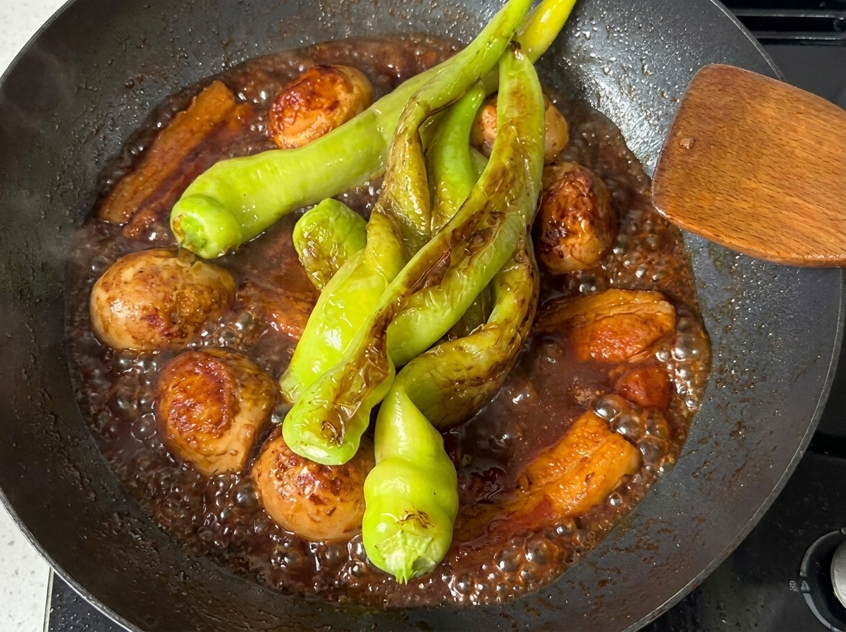 Pimientos verdes cocinándose en la salsa oscura y rica con panceta y huevos duros.