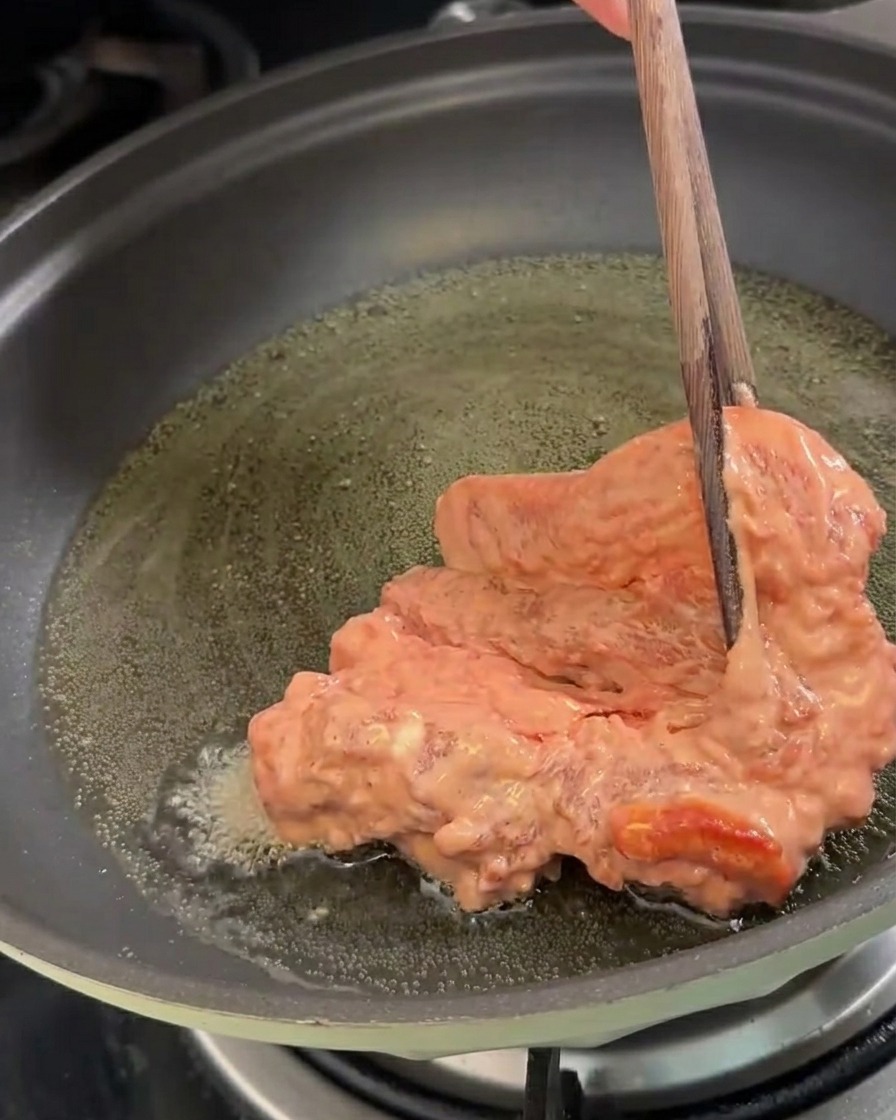 Trozos de cerdo marinados siendo colocados en una sartén con aceite caliente para freír.
