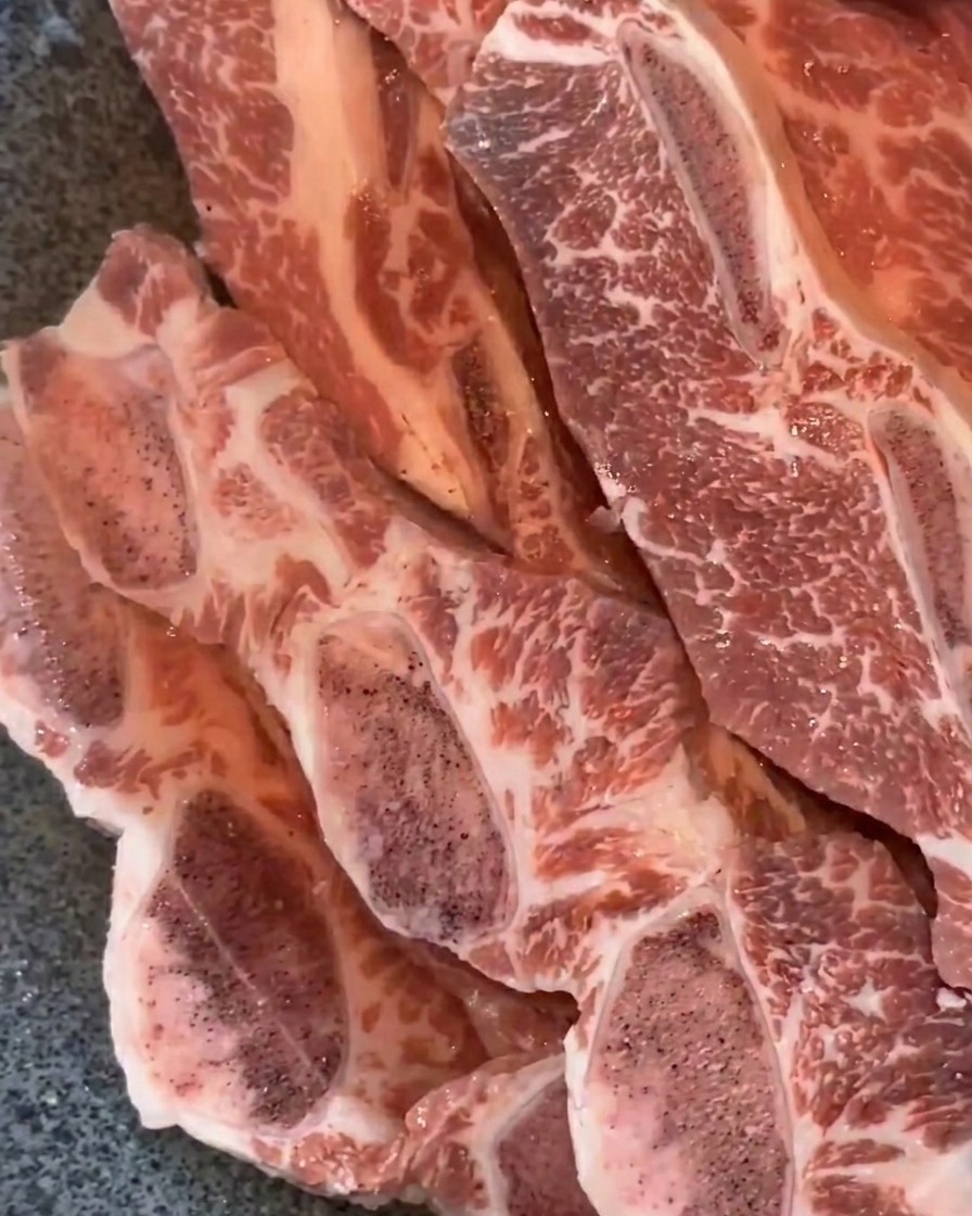 Costillas de res sumergidas en agua en una bandeja de metal.