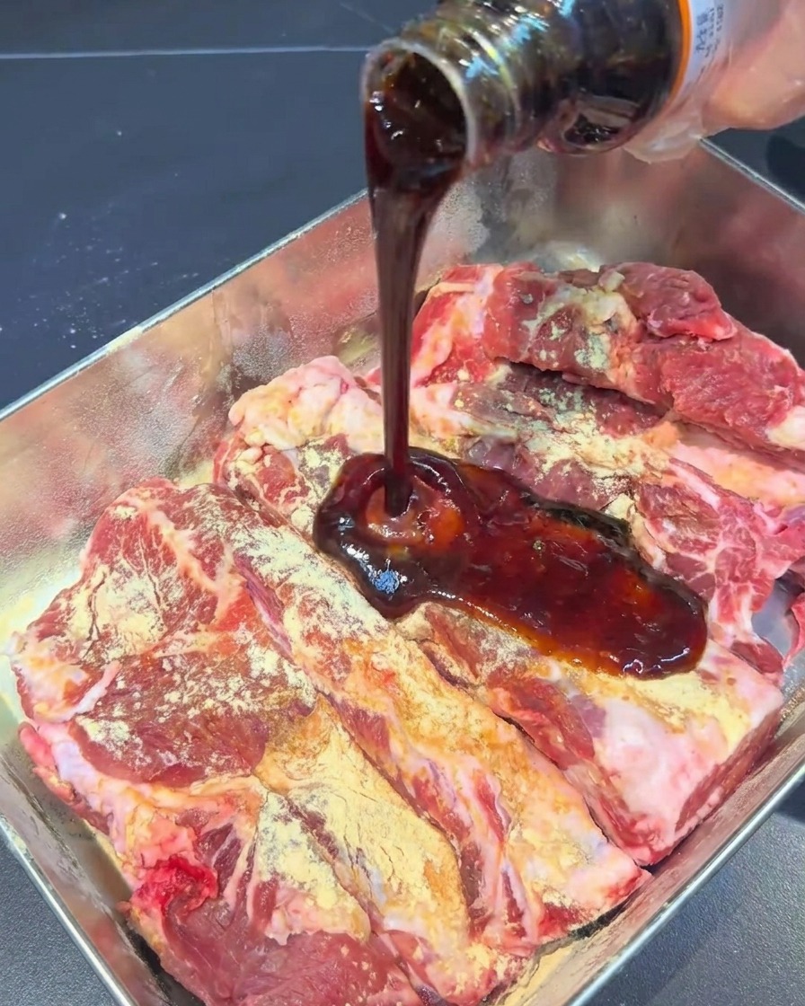 Salsa de marinado oscura siendo vertida desde una botella sobre las costillas.