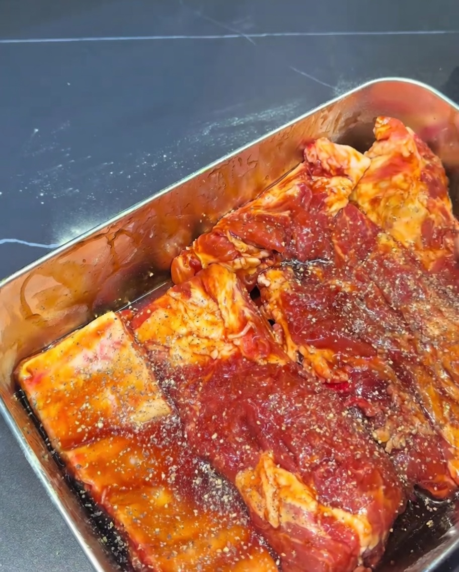 Primer plano de costillas crudas cubiertas de marinado y espolvoreadas con pimienta negra molida.