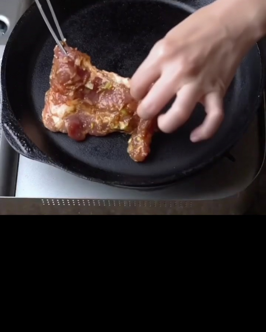 Costillas de cerdo marinadas chisporroteando en una sartén de hierro fundido precalentada.