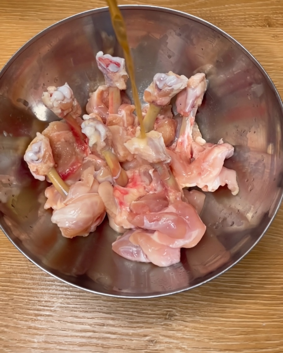 Muslos de pollo sazonados en un tazón de metal con vino de arroz, especias y huevo líquido.