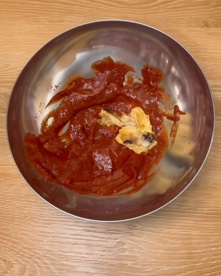 Muslos de pollo horneados siendo mezclados con una rica salsa roja estilo coreano en un tazón de acero inoxidable.