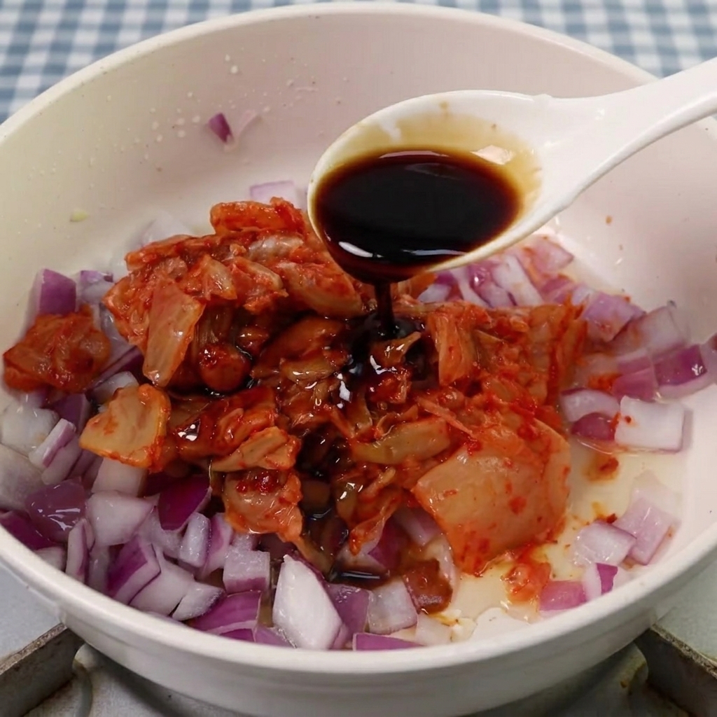 Salsa de soja, azúcar y pasta picante coreana siendo añadidas a la mezcla de kimchi y cebolla.