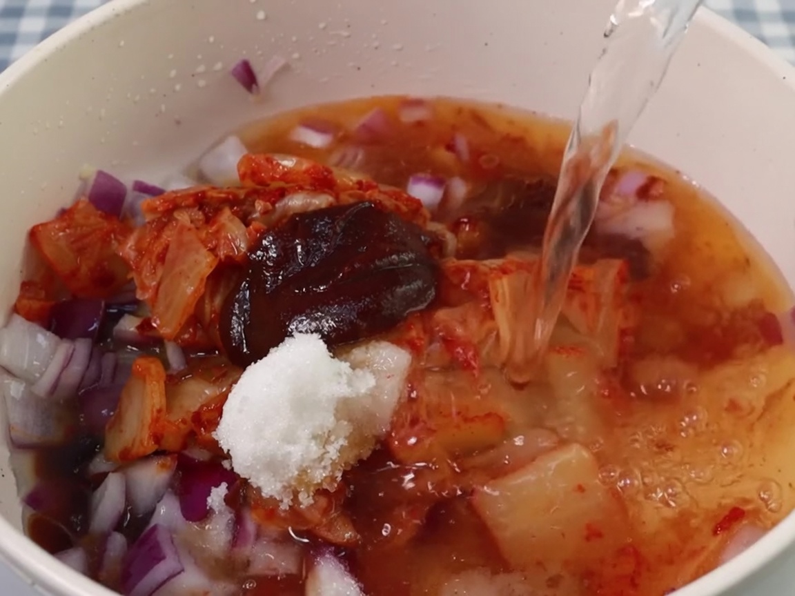 Agua siendo vertida en la olla con la base de kimchi y condimentos.