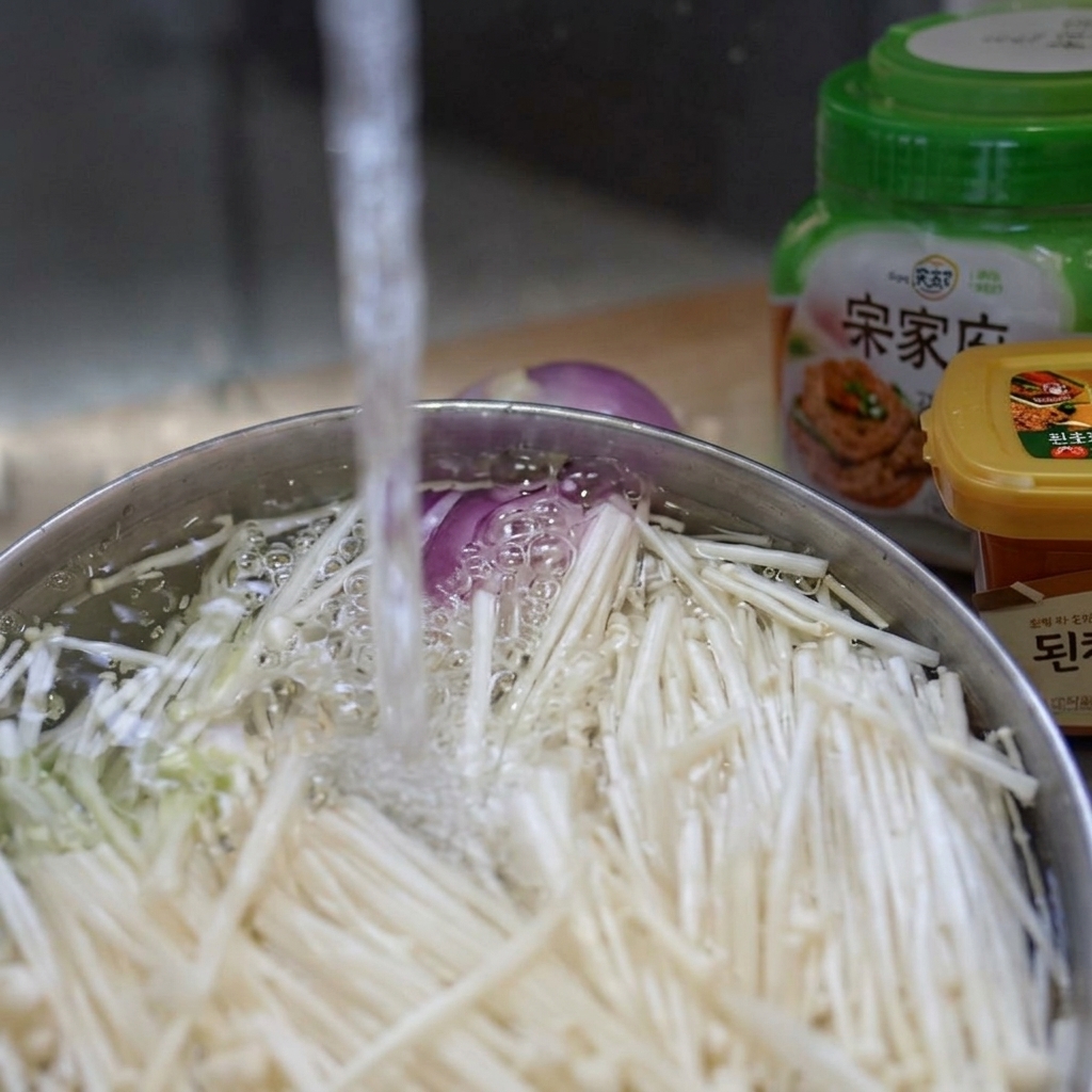 Champiñones enoki siendo lavados en un cuenco bajo un chorro de agua fría.