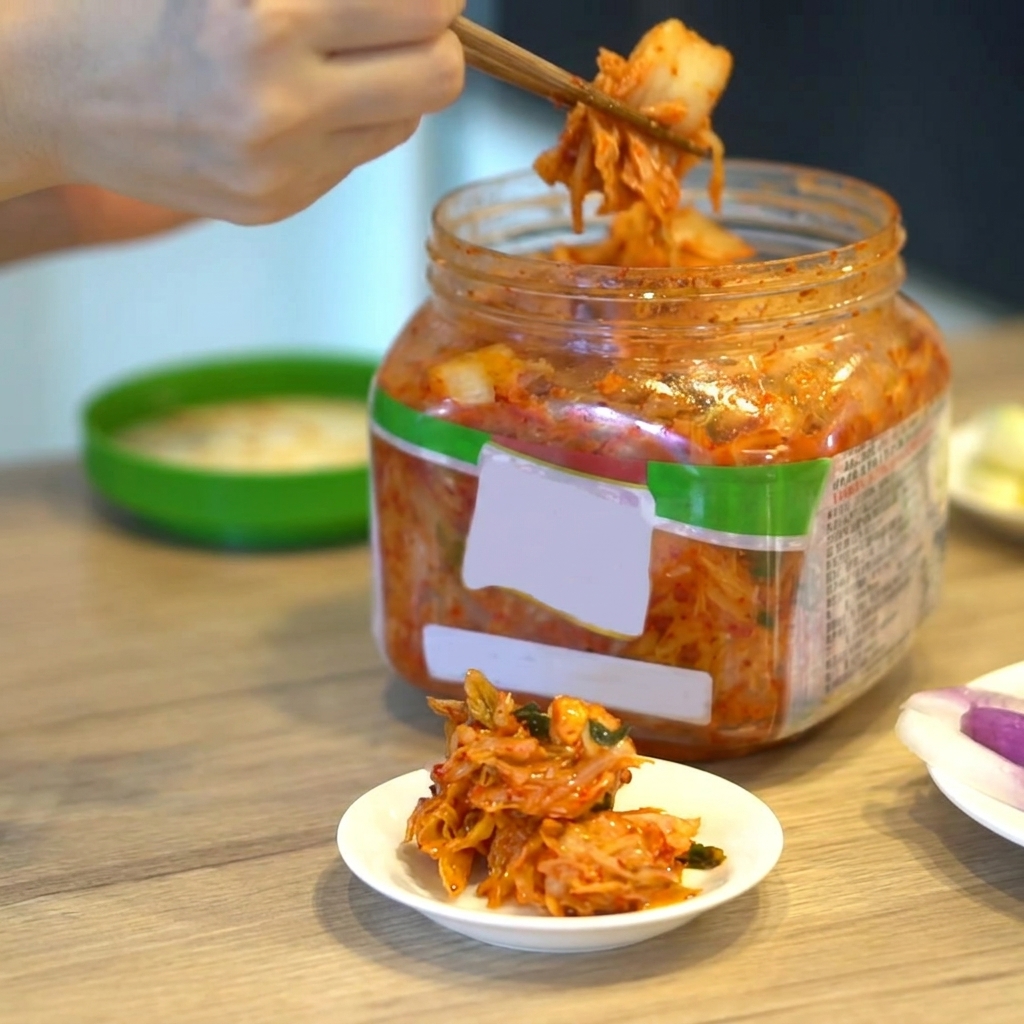 Una porción de kimchi coreano siendo levantada de un recipiente con palillos.