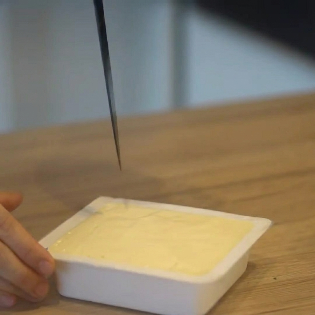 Tofu siendo cortado en cubos mientras aún está en su paquete de plástico.