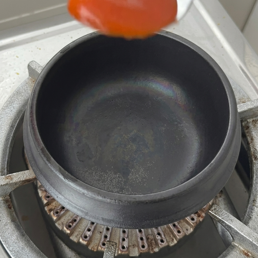 Una cucharada de salsa de chile rojo colocada en el fondo de una olla de barro negra seca sobre una estufa.