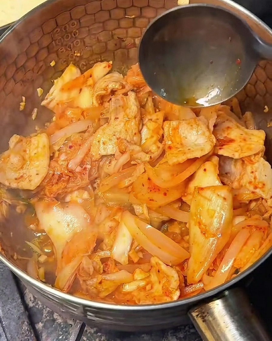 Salsa de soja clara siendo vertida sobre la mezcla de kimchi y cerdo.
