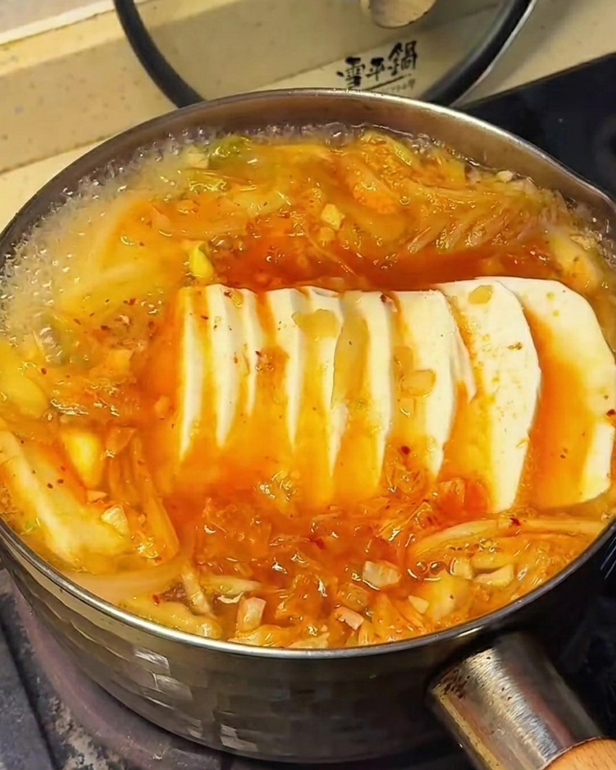 La superficie de la sopa de kimchi con tofu, mostrando el momento en que se esparcen los condimentos.