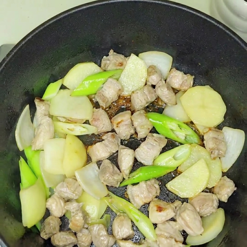 Kimchi fresco siendo incorporado a la base de cerdo y cebolla salteados.
