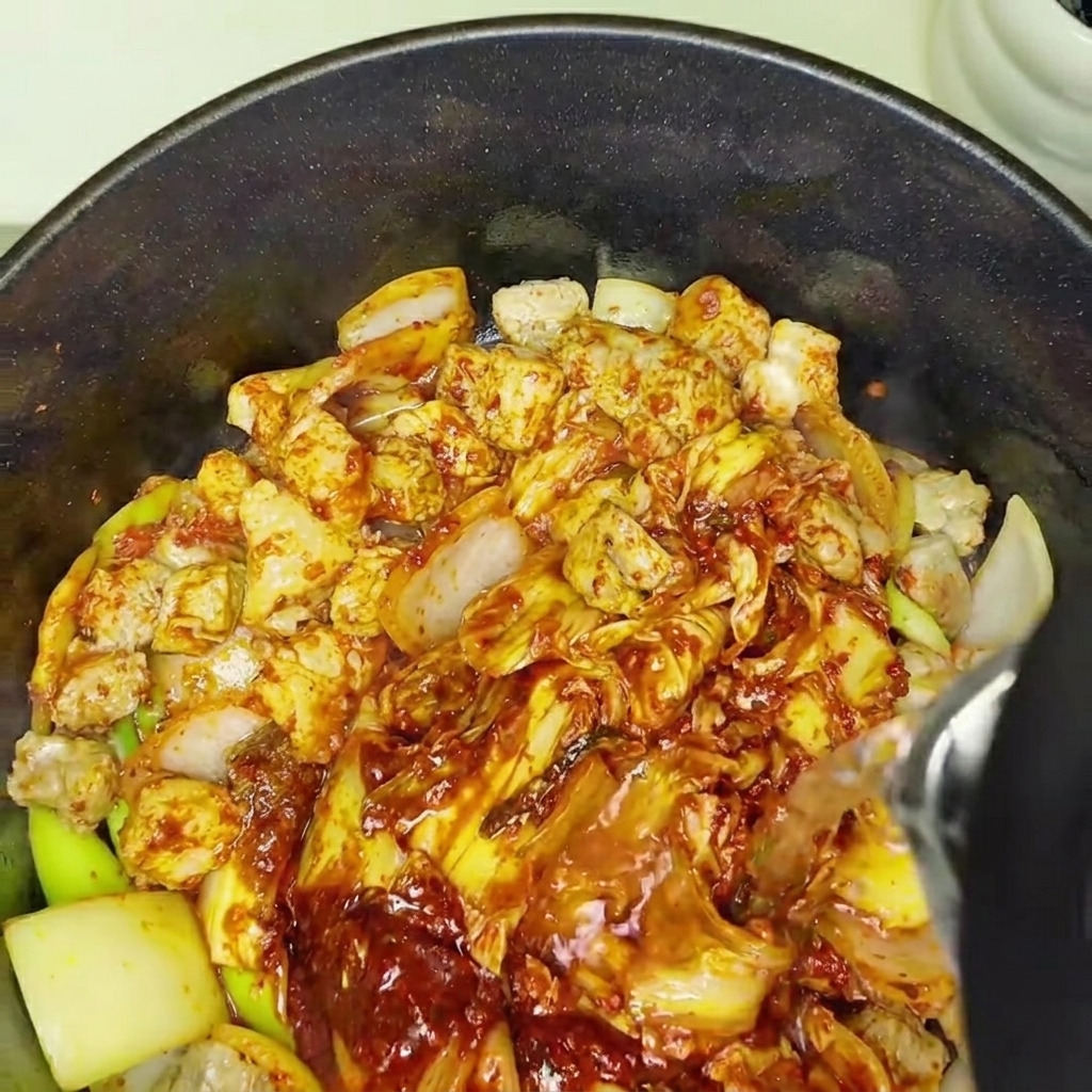 Agua siendo añadida a la olla con el kimchi y el cerdo, iniciando el proceso de cocción a fuego lento.