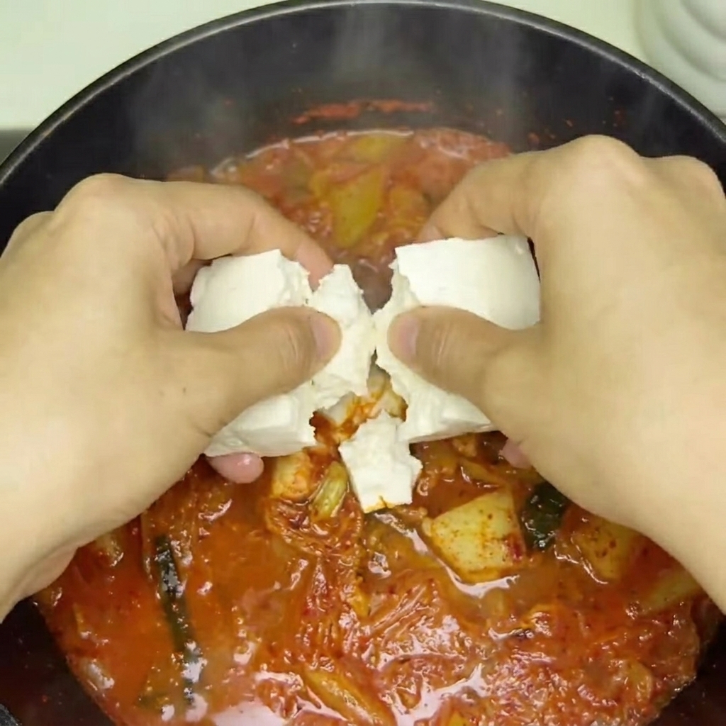 Cubos de tofu fresco siendo colocados en la sopa de kimchi burbujeante.