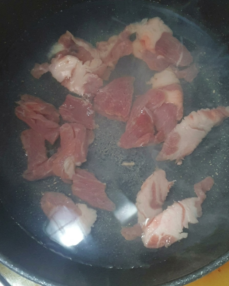 Trozos de cerdo sumergidos en agua en una olla con una cucharada de camarones salados añadida.