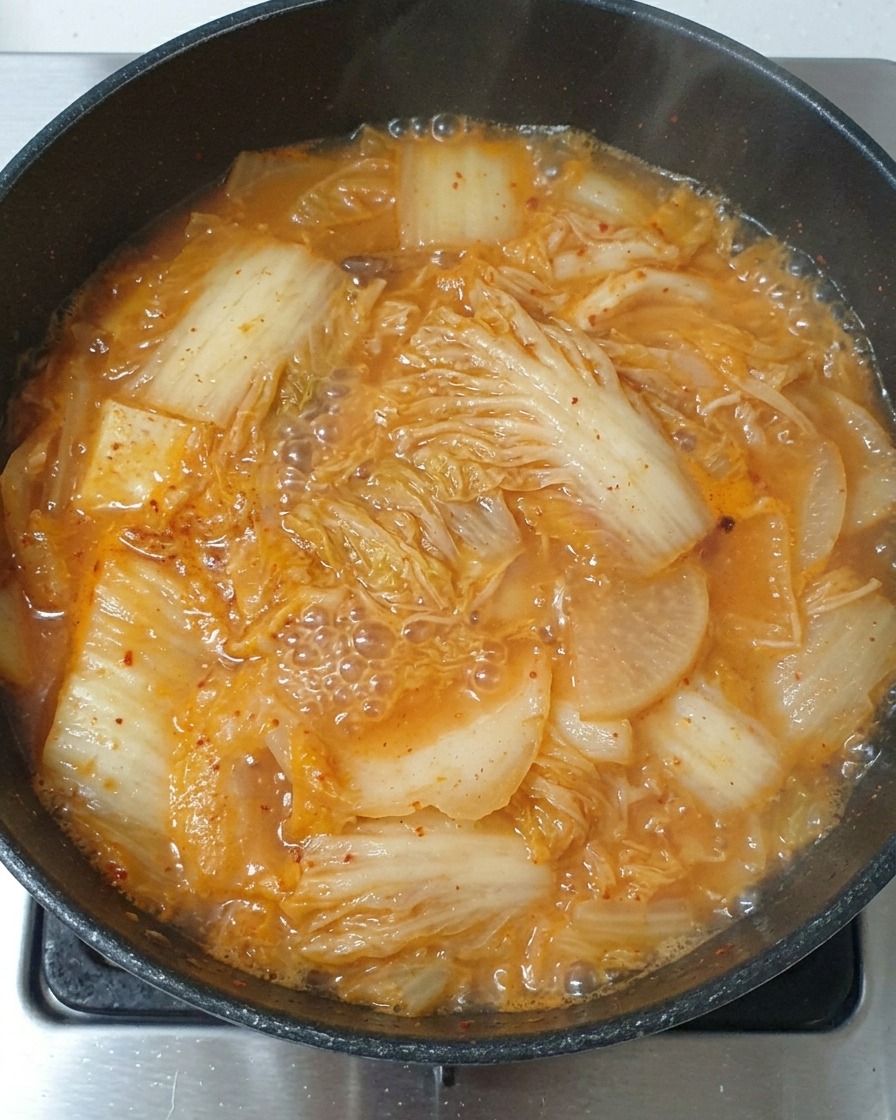 Una cucharada de salsa de soja clara siendo vertida en el estofado de kimchi hirviendo.