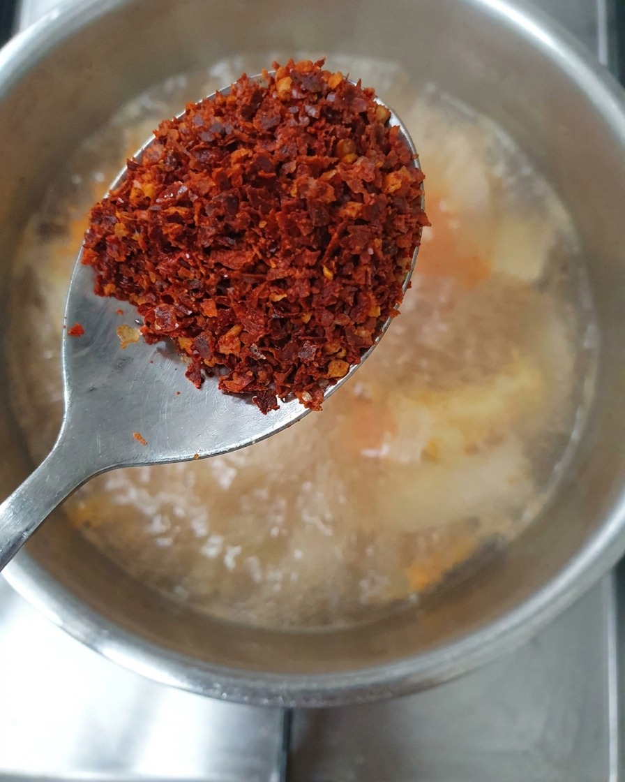 Una cuchara que contiene una mezcla de copos de chile rojo gruesos y finos sobre el estofado.