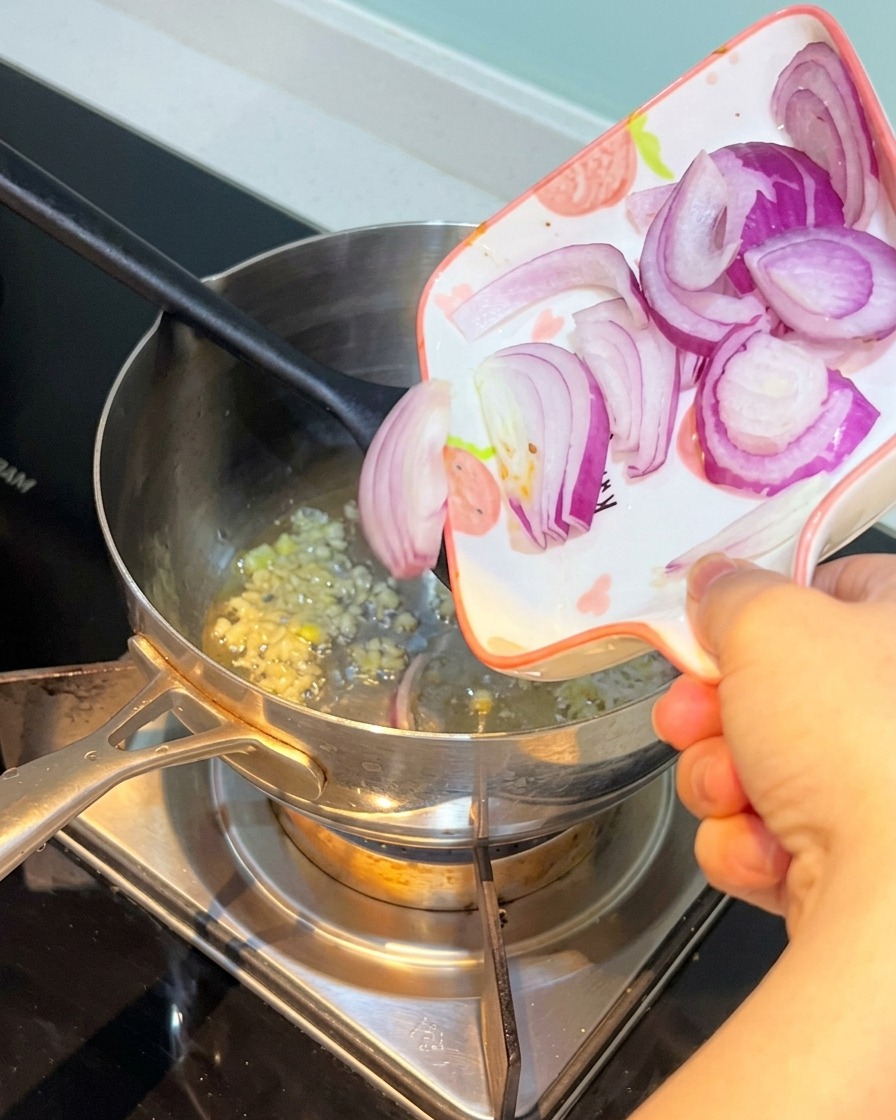 Cebolla morada en rodajas siendo añadida a la olla con el ajo.