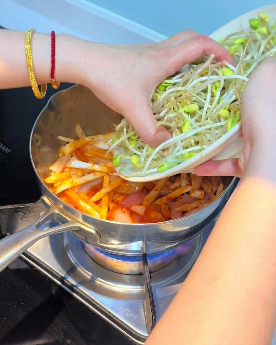 Brotes de soja frescos siendo puestos sobre la mezcla de kimchi y setas.