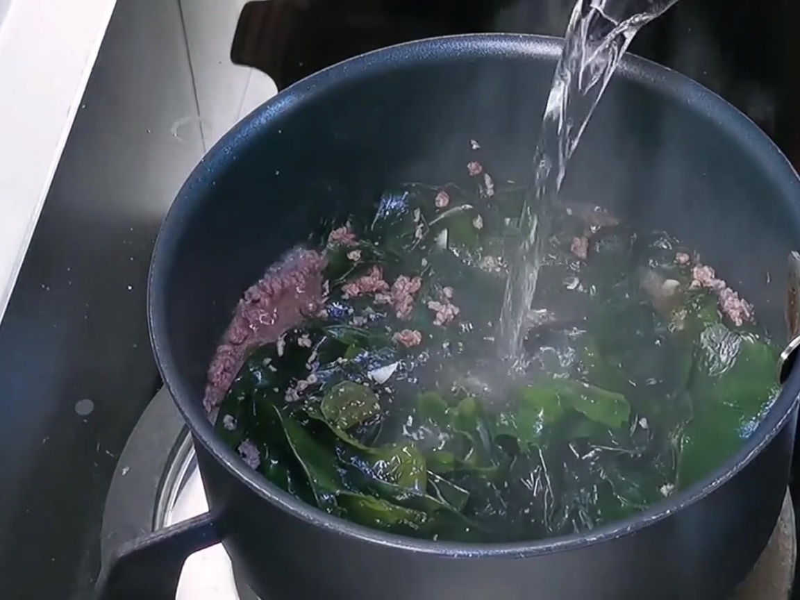 Agua fresca siendo vertida en la olla sobre la base de carne y wakame.