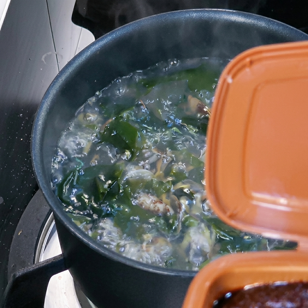 Una cucharada de pasta de soja coreana siendo disuelta en la sopa hirviendo.
