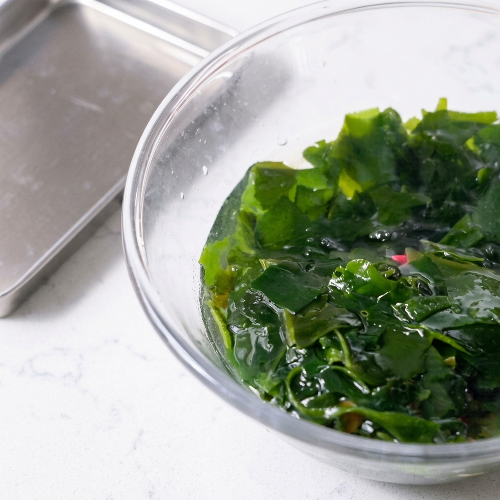 Alga wakame rehidratada siendo extraída de un bol con una cuchara ranurada rosa.