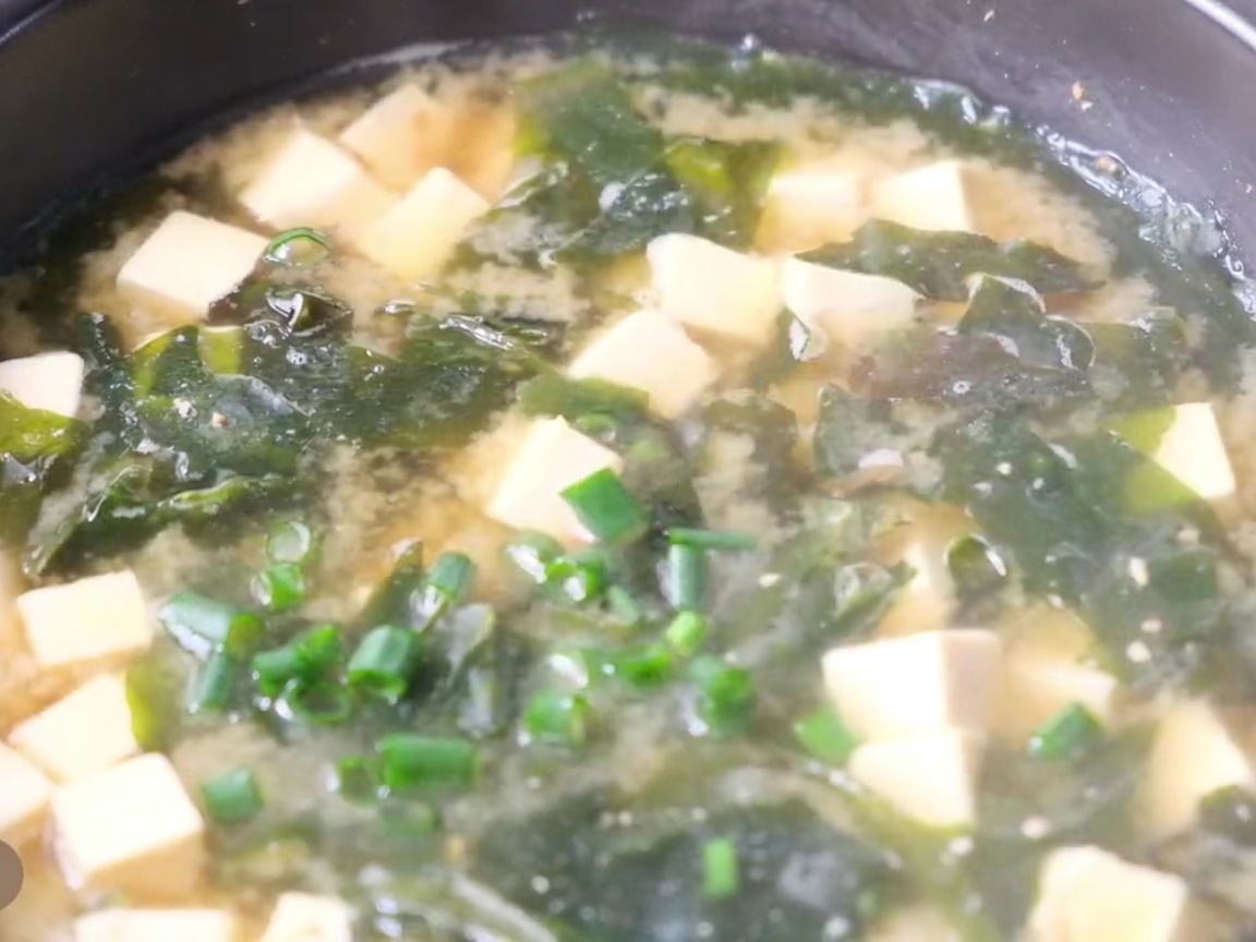 Primer plano de una olla de sopa de miso caliente con cubos de tofu, alga y cebolleta fresca espolvoreada por encima.