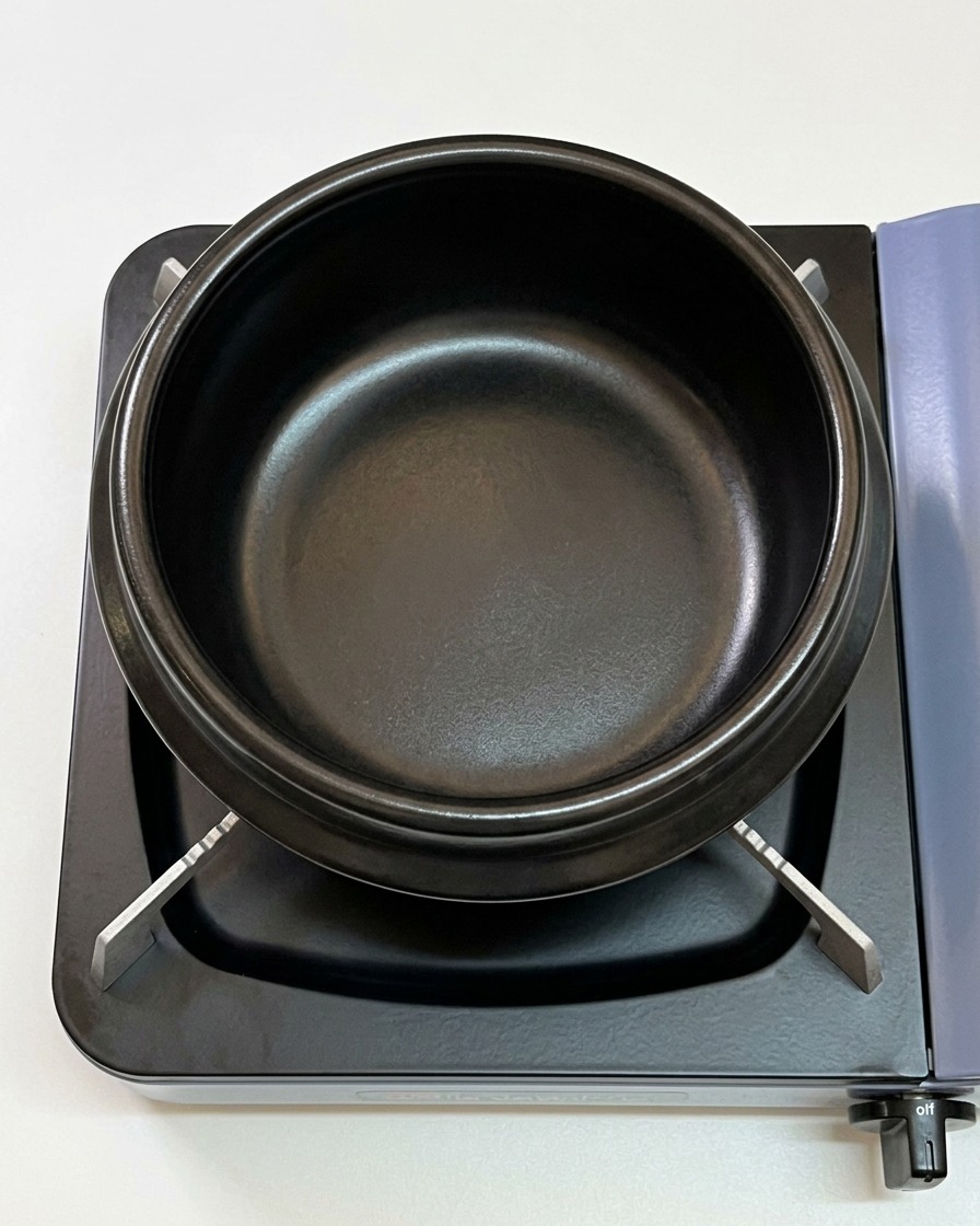 Aceite de sésamo acumulándose en el fondo de una olla de barro negra sobre una estufa.