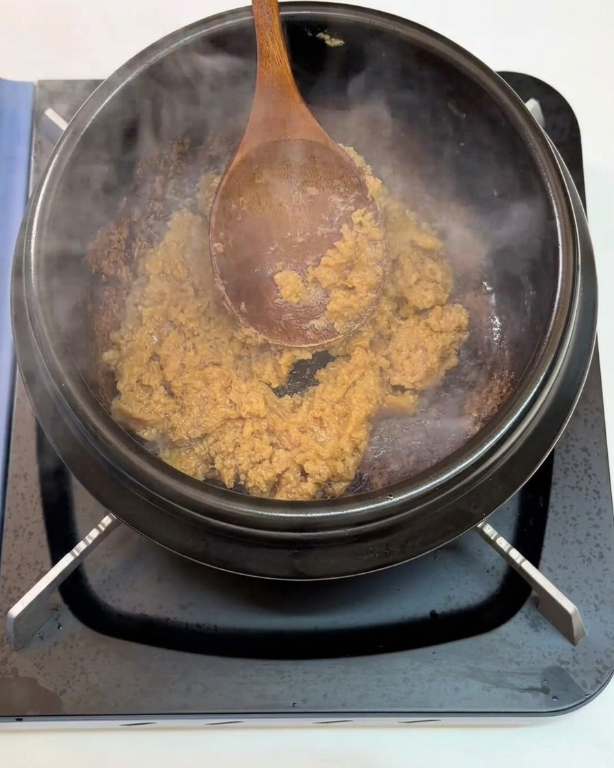 Ajo picado siendo incorporado a la pasta de soja que se sofríe en la olla.
