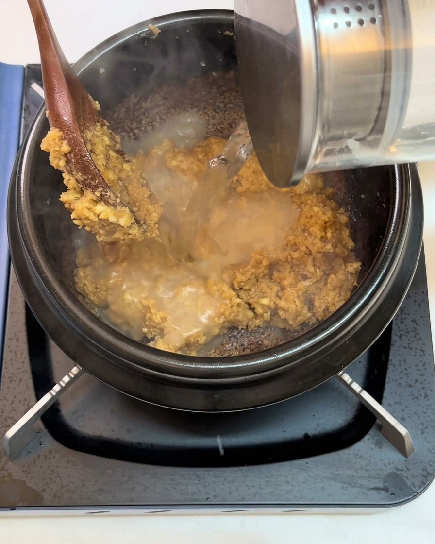 Agua siendo vertida en la olla sobre la mezcla de pasta de soja frita y ajo.
