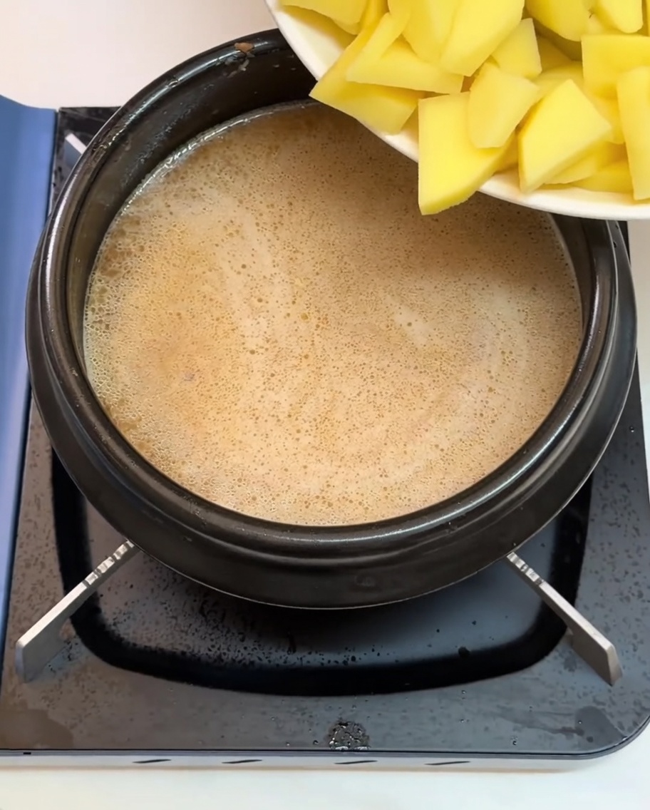 Patatas y varios otros ingredientes picados siendo añadidos al caldo hirviendo.