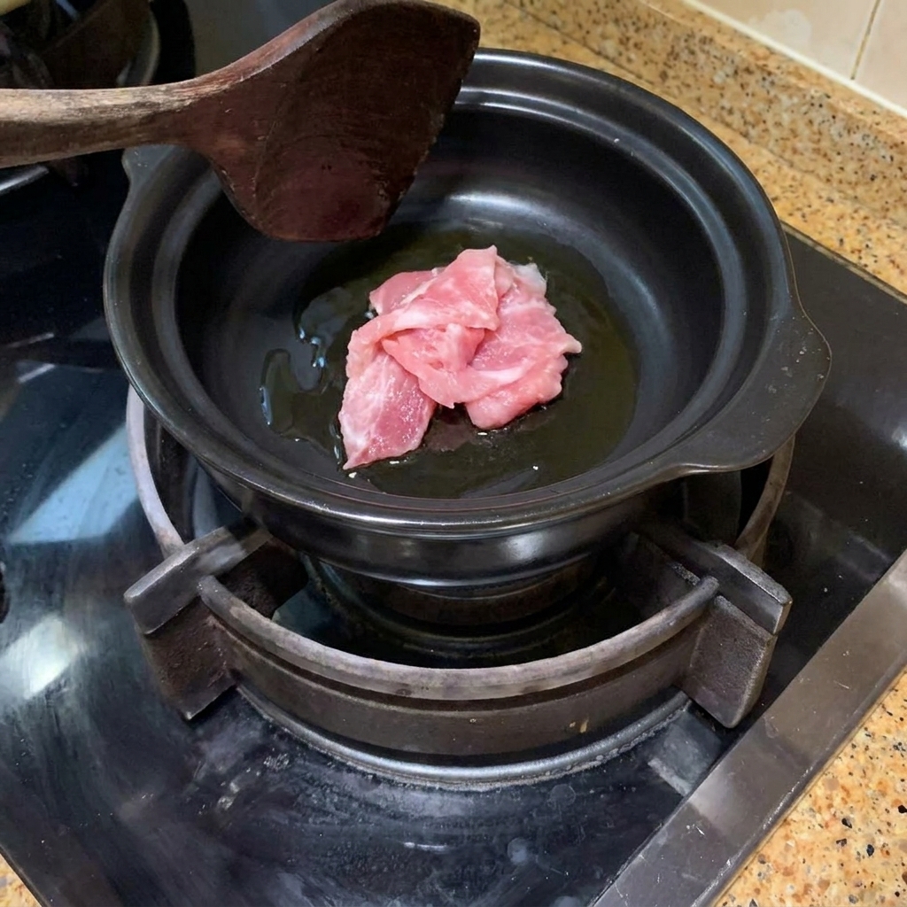 Láminas de cerdo siendo salteadas en una olla de barro caliente con aceite.