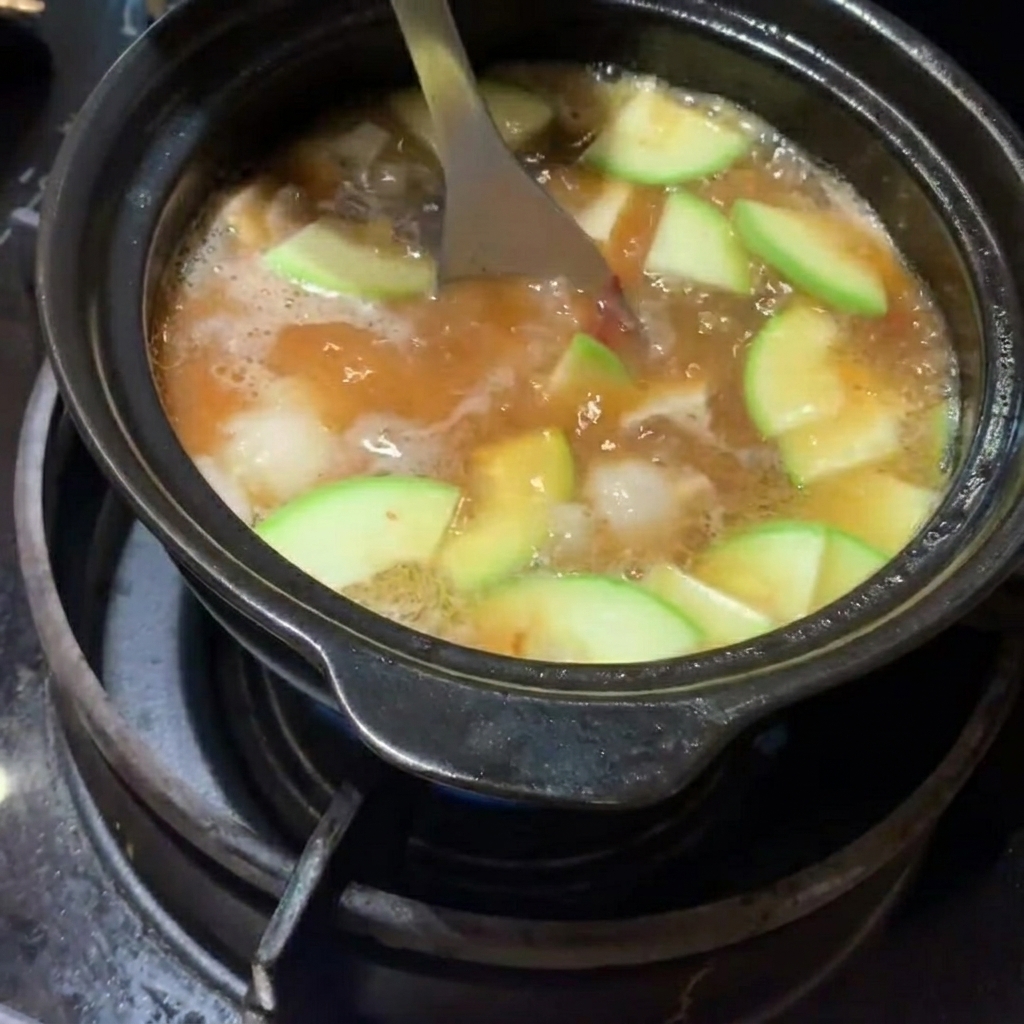 Calabacín en rodajas y patatas en cubos siendo añadidos al estofado.