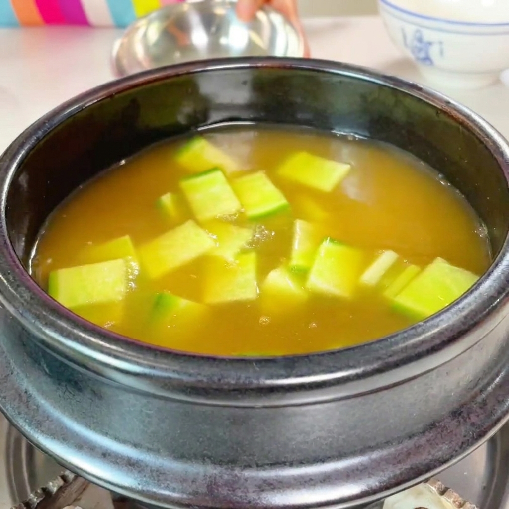 Calabacín verde en cubos y champiñones laminados siendo añadidos a la olla en ebullición.