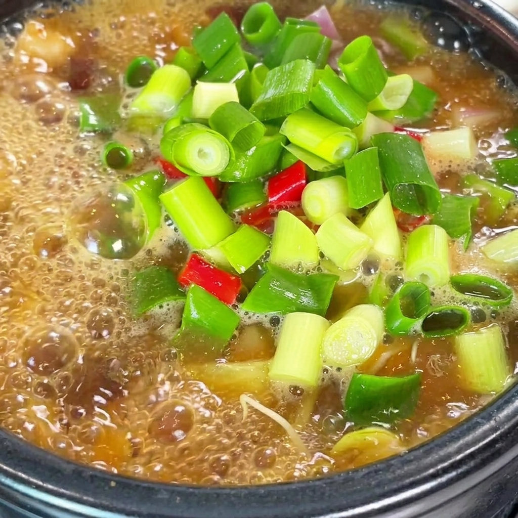 Primer plano del estofado de pasta de soja hirviendo, siendo sazonado con chile en polvo y caldo de carne en polvo.
