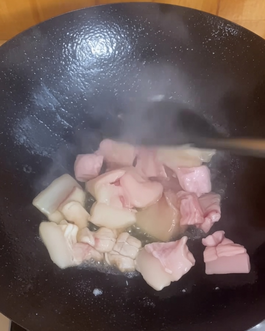 Trozos de panceta sofriéndose y dorándose en un wok caliente.
