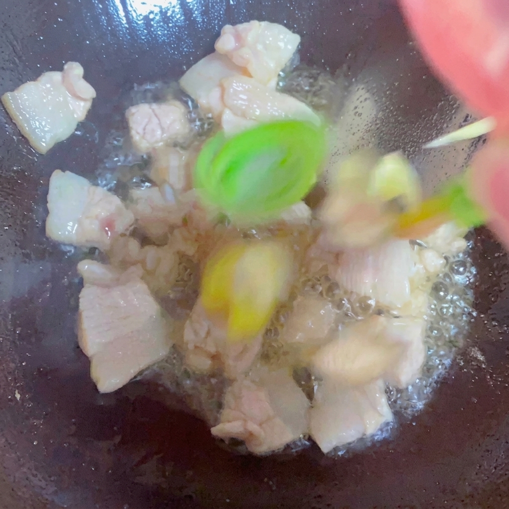 Cebolletas, jengibre y ajo salteándose con la panceta en un wok.