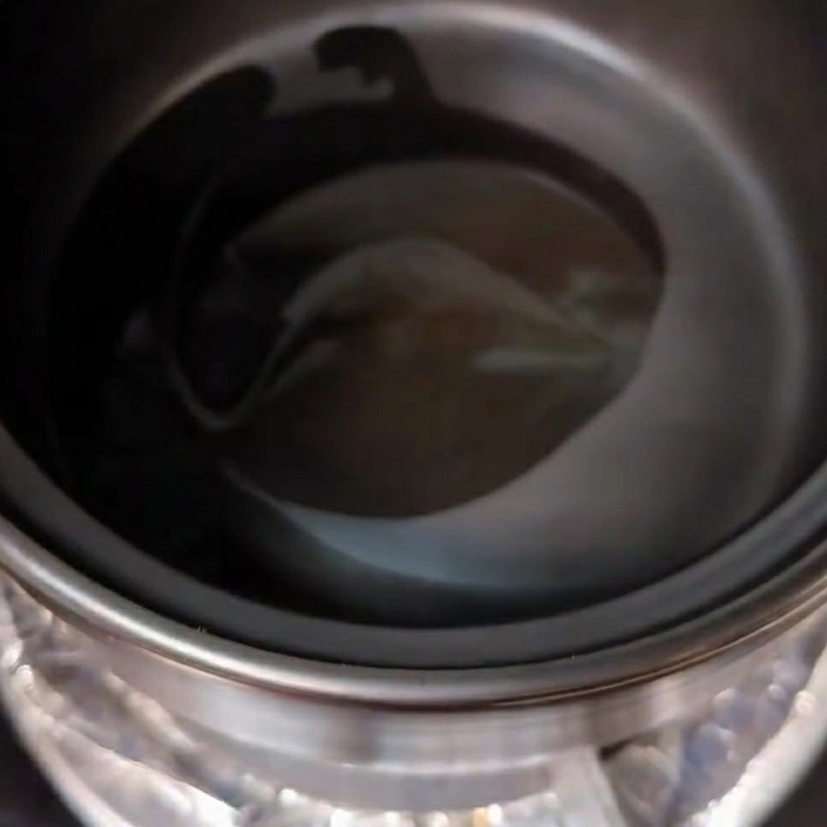 Aceite de cocina y aceite de sésamo aromático vertiéndose con una cuchara en una olla de barro precalentada.