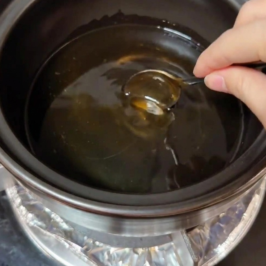 Finas lonchas de panceta dorándose y chisporroteando en aceite caliente dentro de una olla de barro.