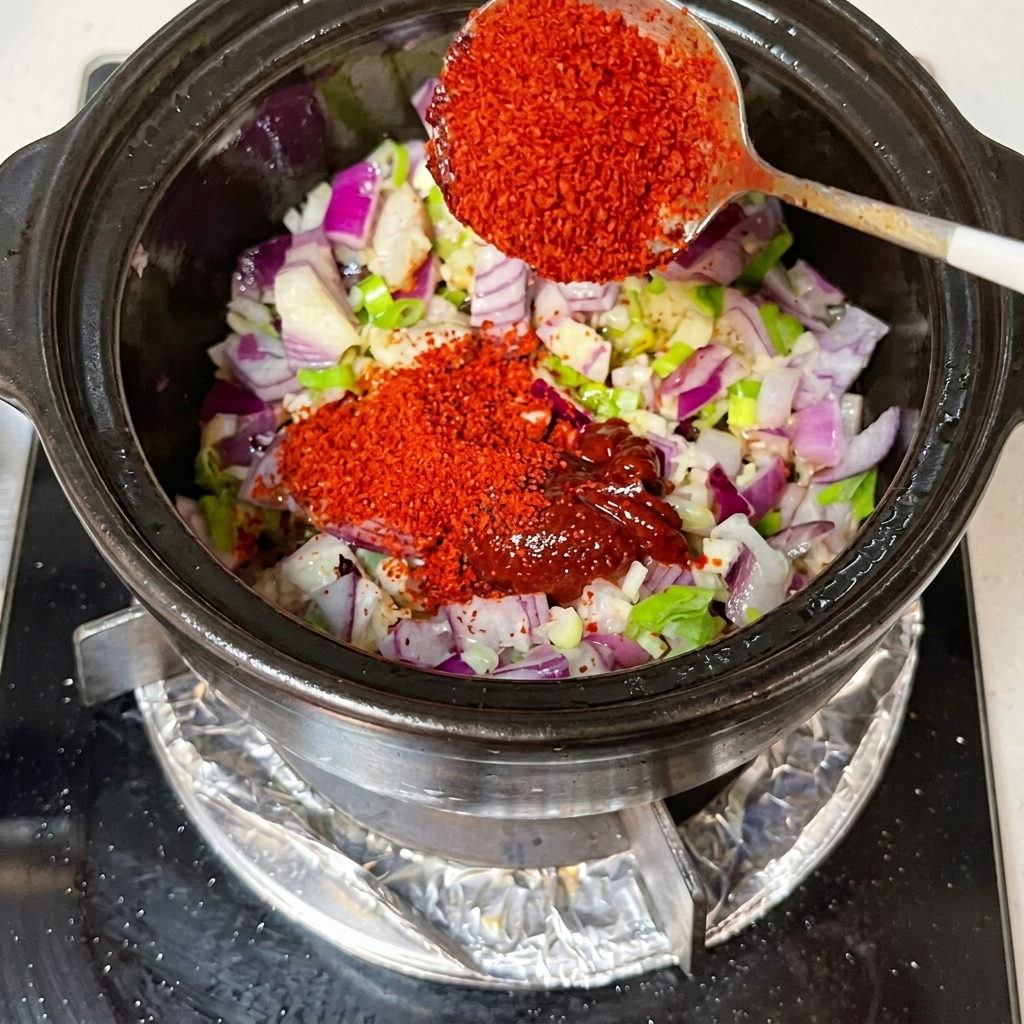 Salsa de soja y kimchi incorporándose a una olla con cebollas picadas y aromáticos.