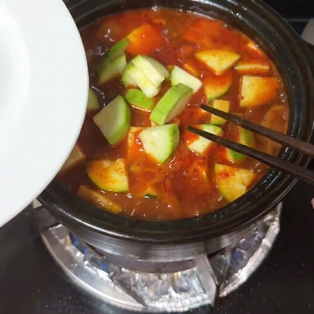 Rodajas de calabacín y cubos de tofu sedoso colocándose en una sopa roja burbujeante.