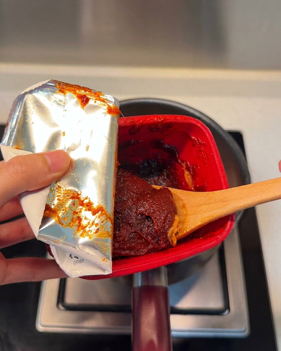 Una cucharada de pasta de chile coreana rica y roja siendo añadida a la olla.