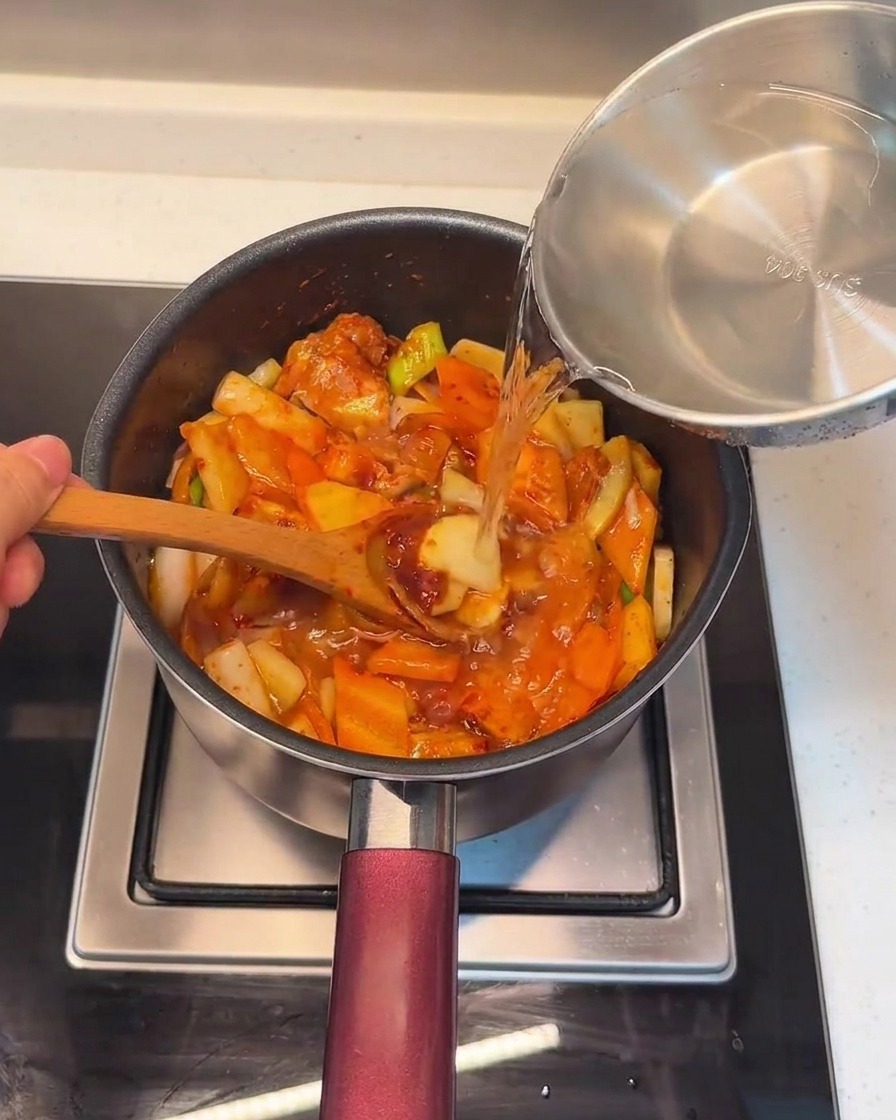 Vertiendo agua fresca en la olla sobre la mezcla combinada de cerdo y verduras.