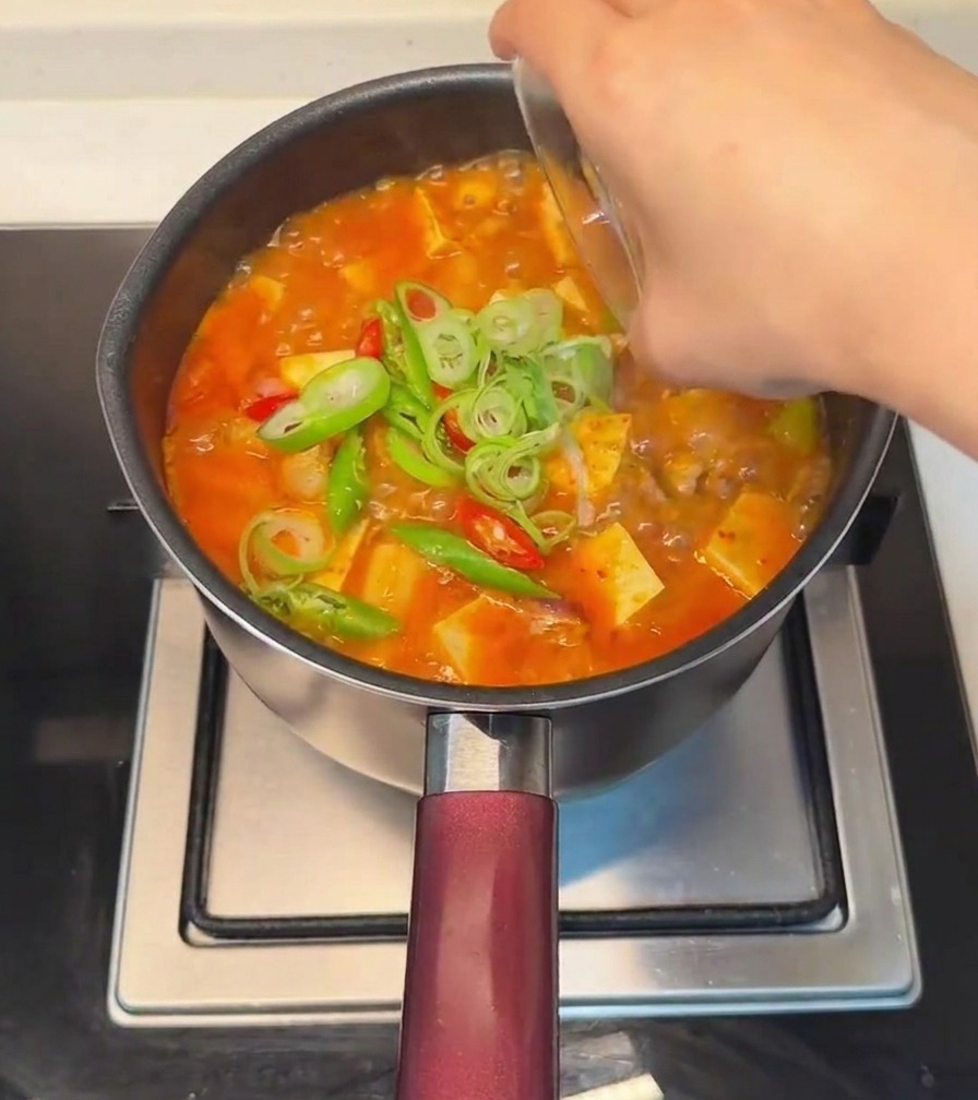 Una mano esparciendo cebollino y chiles rojos y verdes frescos sobre el estofado de tofu terminado.
